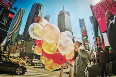 Balloons on Times Square — Photo: Norbert Banhalmi A woman in a denim jacket carries a bunch of red, white and yellow balloons across Times Square.