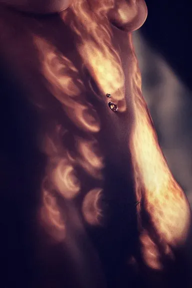 Light on skin — Photo: Norbert Banhalmi An abstract nude study: warm amber light patterns fall across a torso in near darkness.