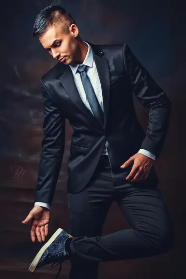 Man in a dark suit — Photo: Norbert Banhalmi Dynamic studio portrait of a man in a dark suit and tie, leaning into the light against a dark background.