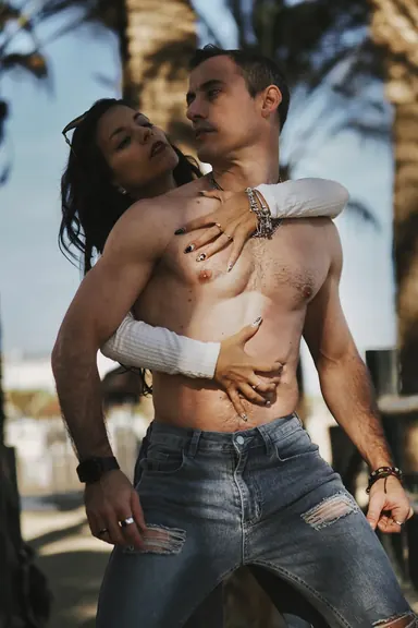 Couple on the shore — Photo: Norbert Banhalmi A couple embraces on a beach at dusk, palm trees behind them.