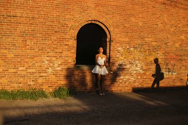 Light in the archway — Photo: Norbert Banhalmi A woman in a white dress stands in a sunlit brick archway while a silhouette passes by.