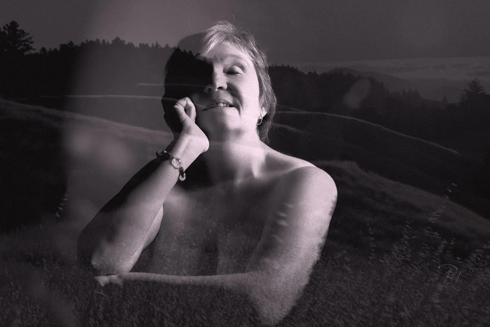 Hills — Photo: Norbert Banhalmi A smiling woman rests her chin on her hand, rolling hills laid over the frame.