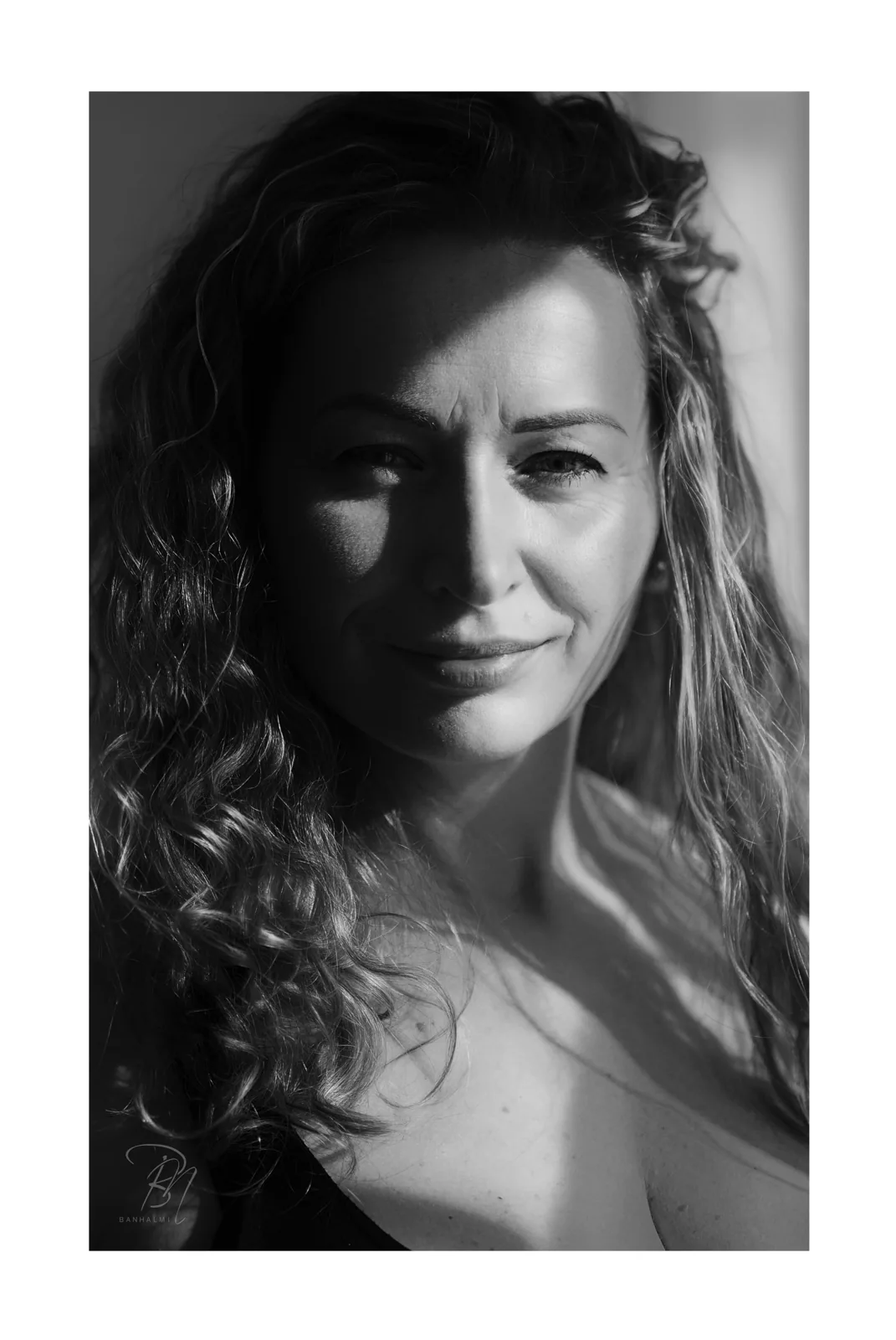 Locken im Seitenlicht — Foto: Norbert Banhalmi Schwarzweißporträt einer Frau mit lockigem Haar, das halbe Gesicht im Schatten.