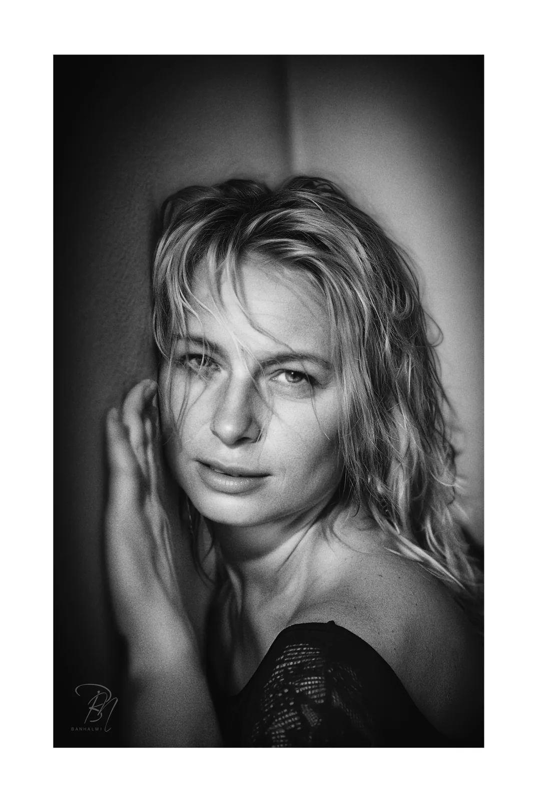 Wand und Schulter — Foto: Norbert Banhalmi Eine Frau lehnt an einer schlichten Wand, die Hand im Haar, die Schulter frei.
