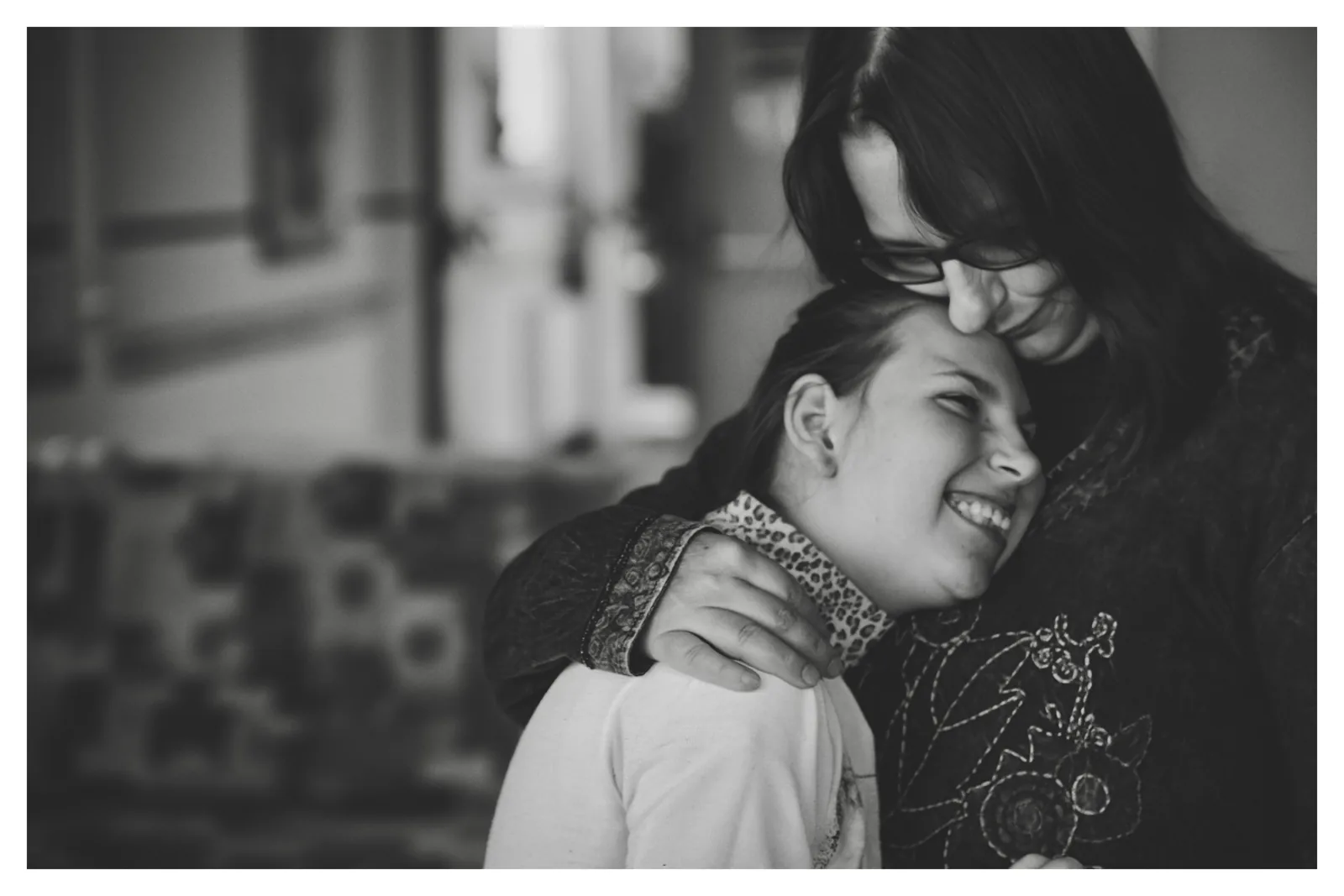Cheek to cheek — Photo: Norbert Banhalmi A woman holds a smiling young woman close, their cheeks almost touching.