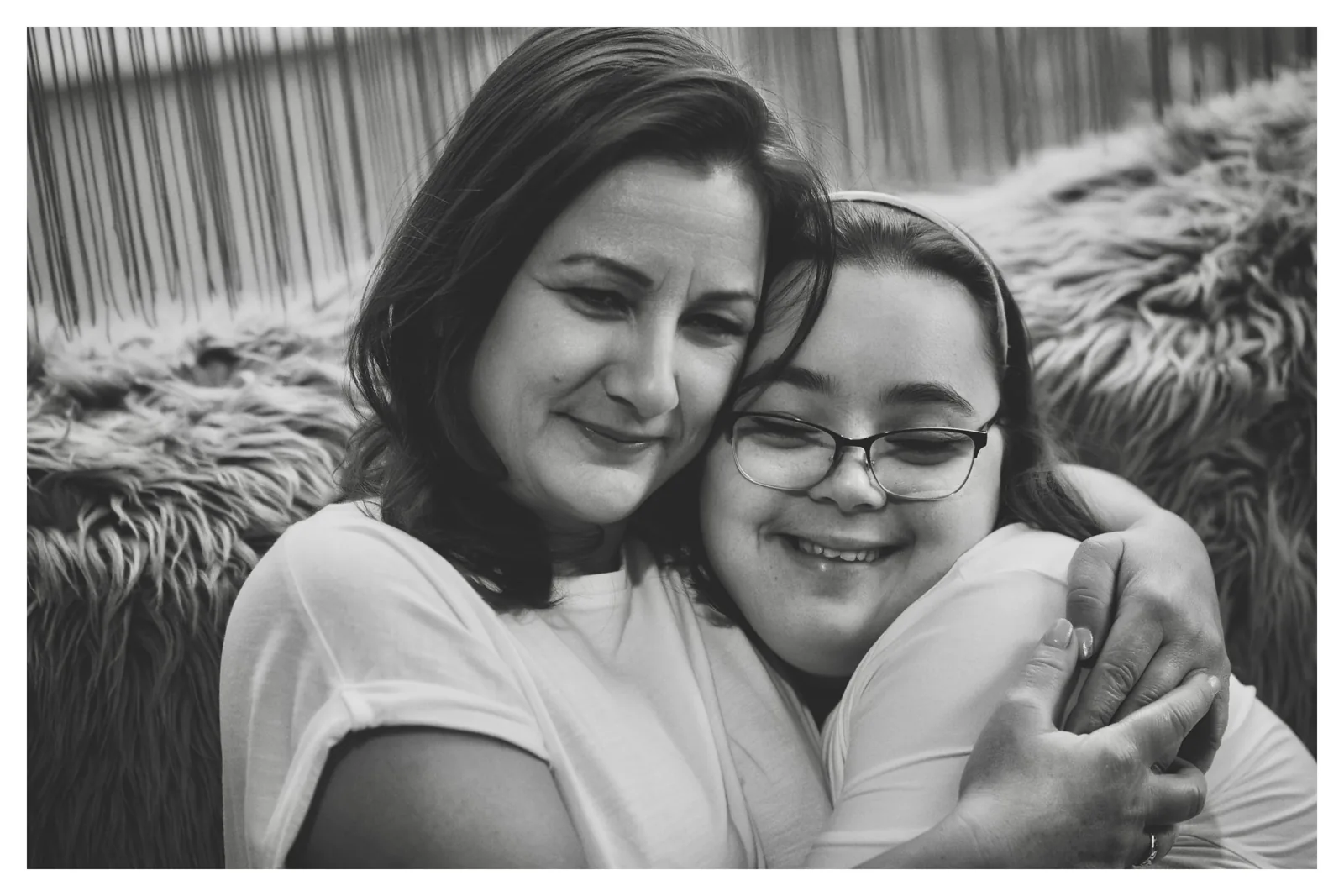 Held close — Photo: Norbert Banhalmi A woman holds a girl in glasses close to her; both are smiling.
