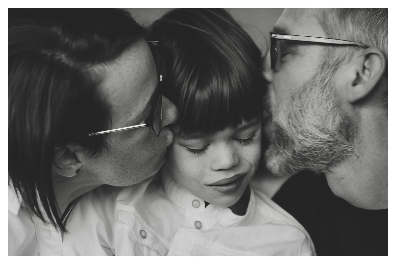 Both sides — Photo: Norbert Banhalmi A woman kisses a girl's forehead while a bearded man leans in from the other side.